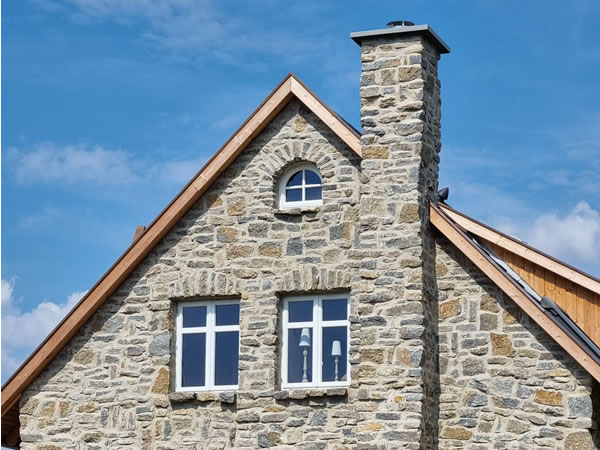 Giebelseite eines englischen Cottages mit Sprossenfenstern, Schornstein und Natursteinfassade
